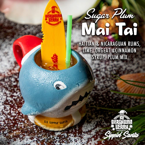 A drink called "Sugar Plum Mai Tai" in a shark mug with a surfboard stirrer, featuring rums and fruit flavors.