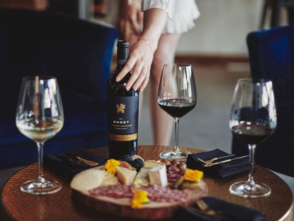 A wine tasting dinner: a bottle and wine glasses with a cheese/charcuterie board on the table, with people in the background.