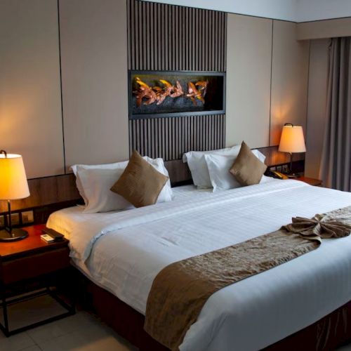 A neatly made hotel room bed with two side tables, lamps, and decorative pillows. The ambiance is warm with a modern design, well-lit and inviting.