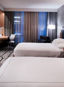 This image shows a modern hotel room with two neatly made beds, a large TV, a desk with a chair, and contemporary decor.