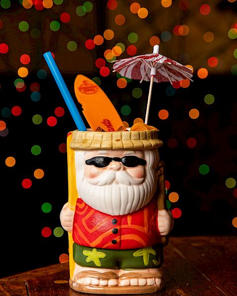 A Santa-style mug drink with sunglasses, straws, and a small umbrella, set against colorful bokeh lights in the background.