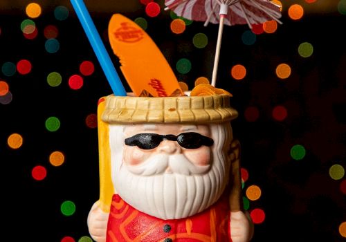 A Santa-style mug drink with sunglasses, straws, and a small umbrella, set against colorful bokeh lights in the background.
