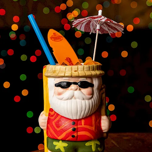 A Santa-style mug drink with sunglasses, straws, and a small umbrella, set against colorful bokeh lights in the background.