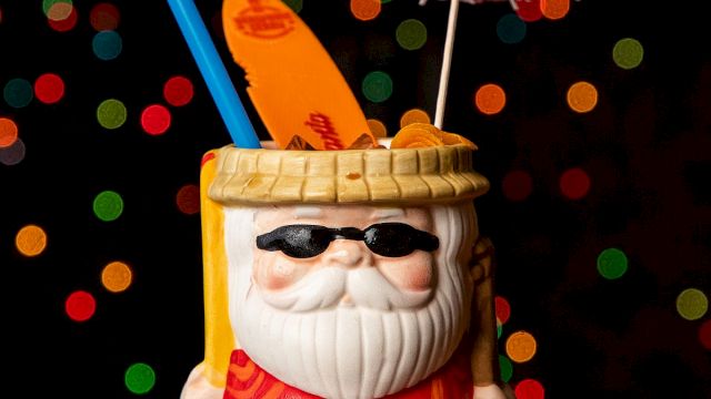 A Santa-style mug drink with sunglasses, straws, and a small umbrella, set against colorful bokeh lights in the background.