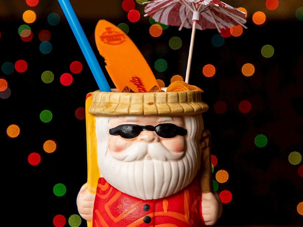 A festive nutcracker-style cocktail with a blue straw and tiny striped umbrella, set against colorful bokeh lights.