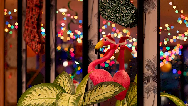 Flamingo decorations sit by a window as colorful city lights blur outside, creating a festive, cozy night scene.