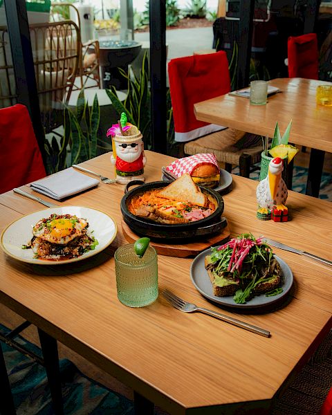 A restaurant patio table with burgers, sizzling skillet dishes, salad, cocktails, and festive mini d&eacute;cor in red seating.