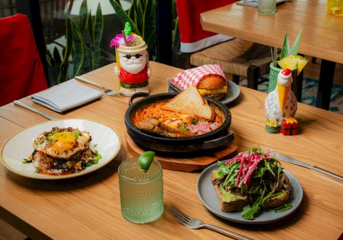 A restaurant patio table with burgers, sizzling skillet dishes, salad, cocktails, and festive mini d&eacute;cor in red seating.
