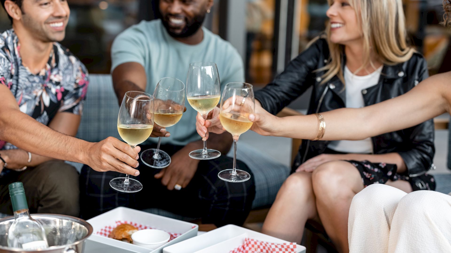People are toasting with glasses of white wine around a table with food containers.