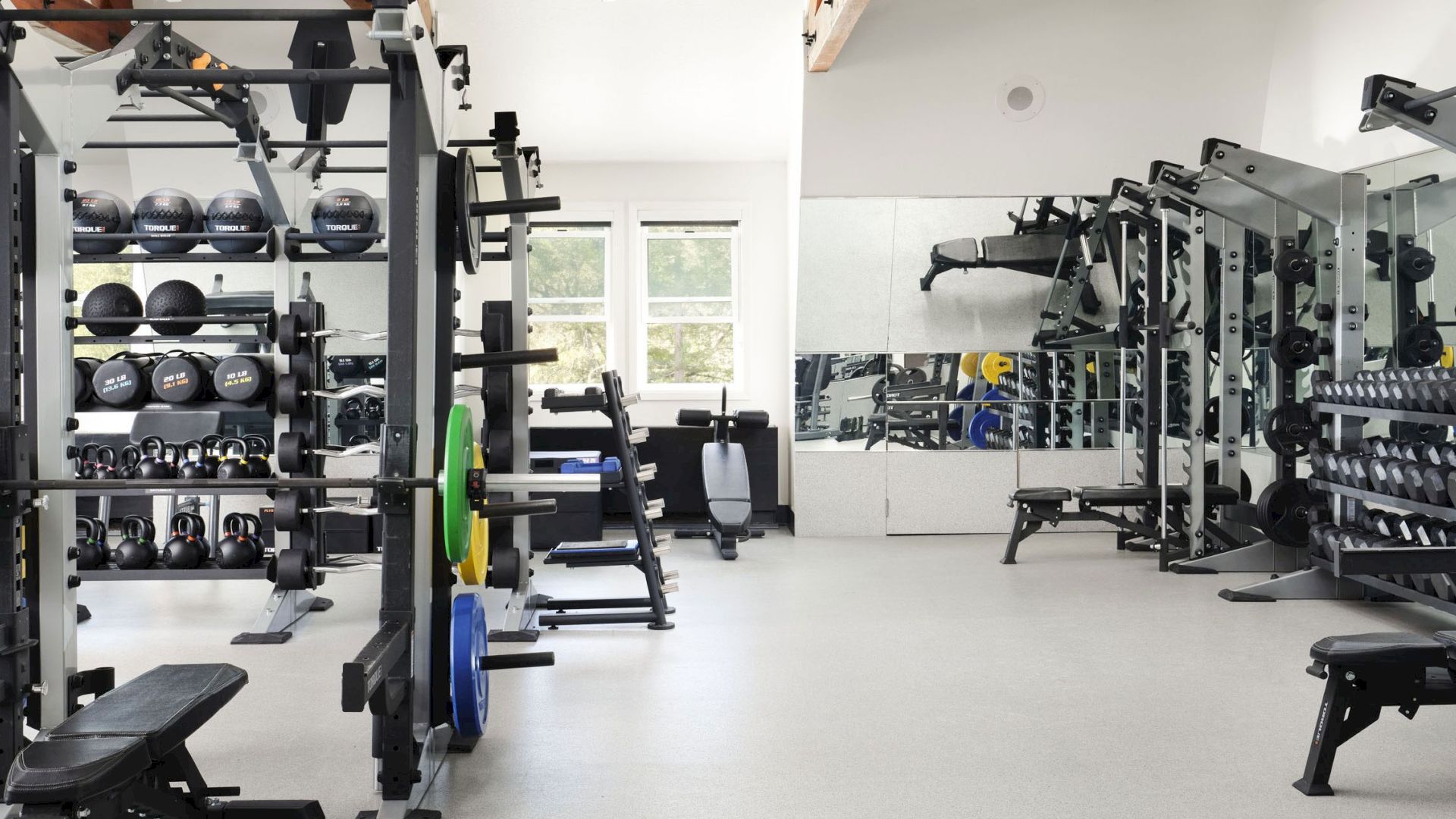 This image shows a well-equipped gym with various weightlifting and exercise machines, free weights, and mirrors on the walls.