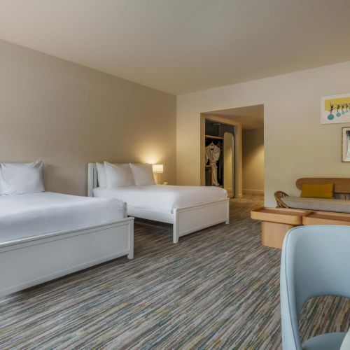 A bright, modern bedroom with a white bed, nightstands, a cozy seating area, and soft decor accents.