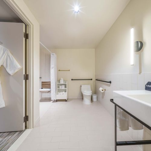 A bright, modern bathroom with a long vanity, double sinks, a large mirror, soft lighting, and a neutral, minimalist color palette.