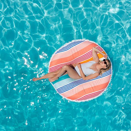 A person in a swimsuit is lounging on a colorful float in a pool, enjoying the sunny day and the refreshing water.