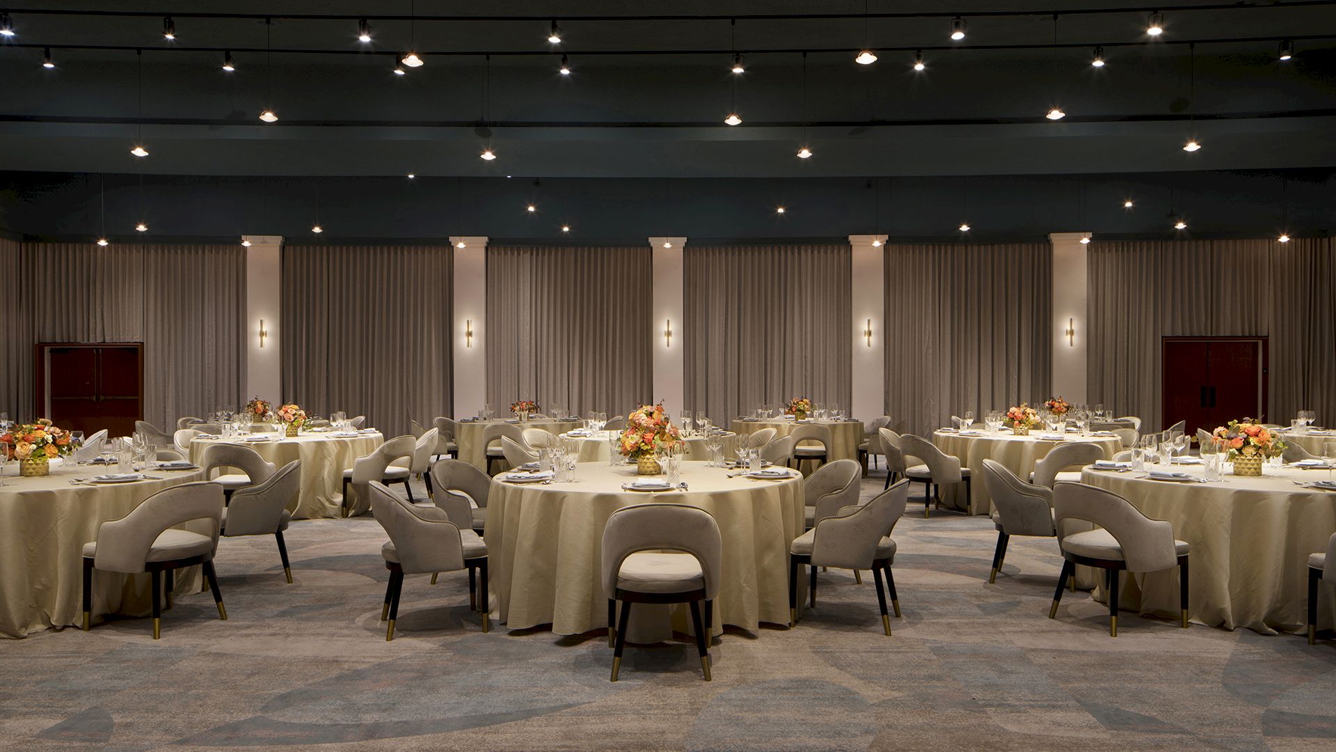 The image shows a banquet hall with round tables set for an event. The room has elegant lighting and floral centerpieces.