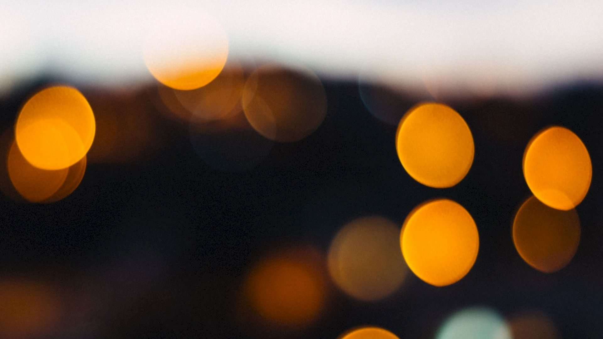 The image features a blurred, bokeh effect with various out-of-focus circular lights in shades of orange and yellow against a darker background.
