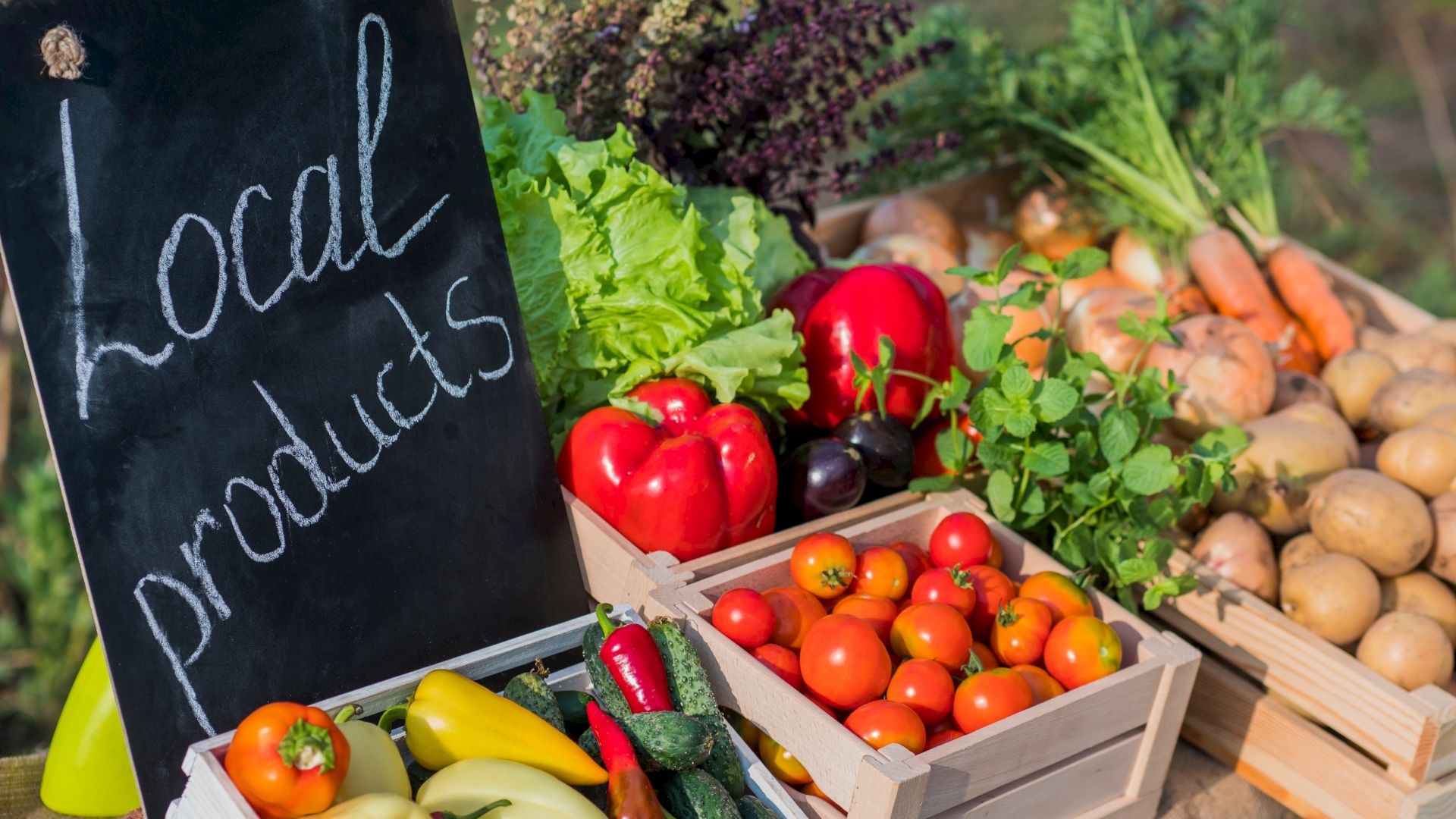 A display of fresh vegetables including tomatoes, peppers, carrots, and lettuce, with a chalkboard sign reading "Local products."