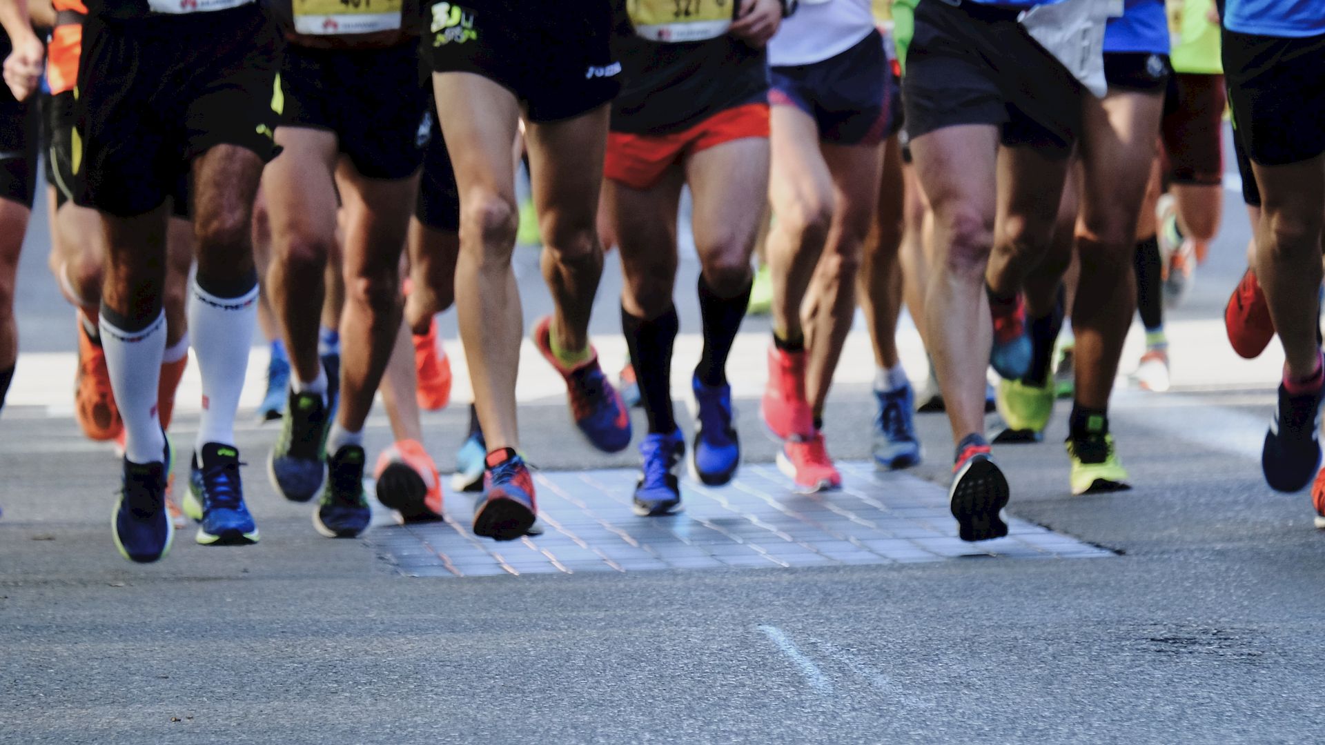 A group of runners in athletic wear are participating in a race, with visible focus on their legs and running shoes as they move forward.