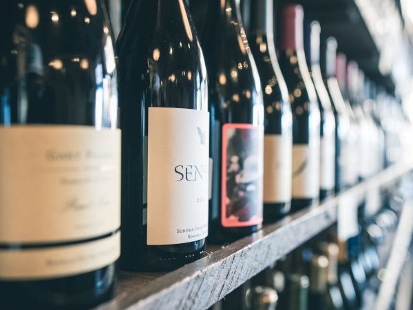 This image shows a row of wine bottles lined up on a shelf, each with distinct labels, in what appears to be a wine shop or bar setting.
