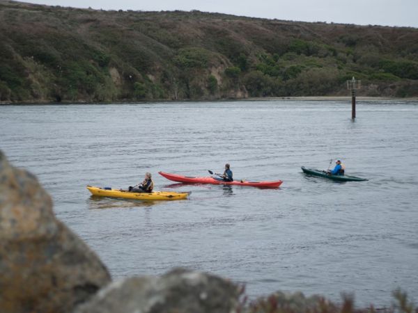 Three people are kayaking on a body of water with a hilly landscape in the background.