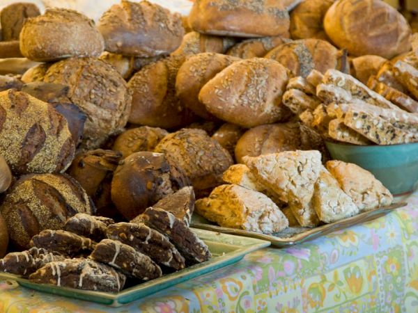 The image shows an assortment of freshly baked bread and pastries arranged on a table, including loaves, scones, and cookies.