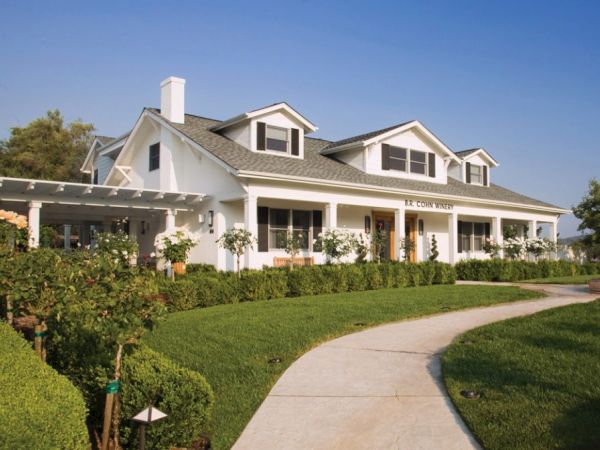 A large white house with dormer windows, a wraparound porch, and well-maintained landscaping, including hedges and a curved pathway ending the sentence.