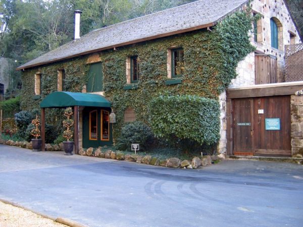An ivy-covered building with a green awning over the entrance, a wooden door, and surrounding greenery in a rural setting, is shown.