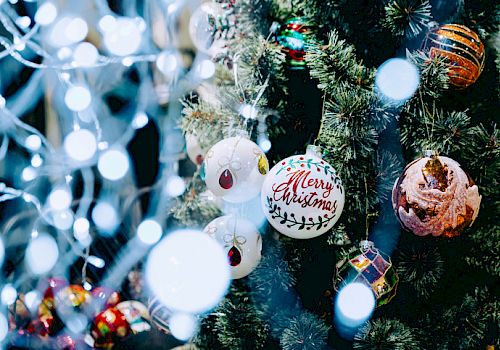 A decorated Christmas tree with various ornaments, including a "Merry Christmas" bauble, surrounded by festive lights and decorations.