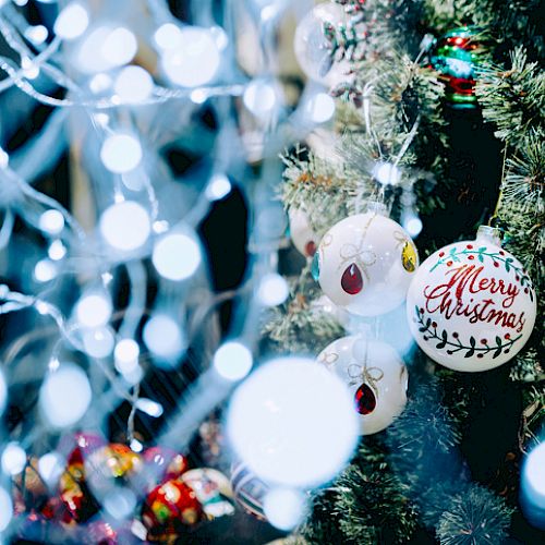 A decorated Christmas tree with various ornaments, including a "Merry Christmas" bauble, surrounded by festive lights and decorations.
