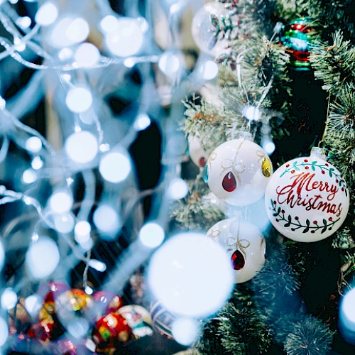 A decorated Christmas tree with various ornaments, including a "Merry Christmas" bauble, surrounded by festive lights and decorations.