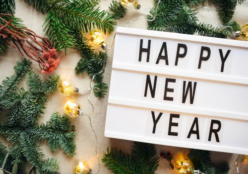 A lightbox sign says "HAPPY NEW YEAR" surrounded by green pine branches and festive string lights, creating a celebratory atmosphere.