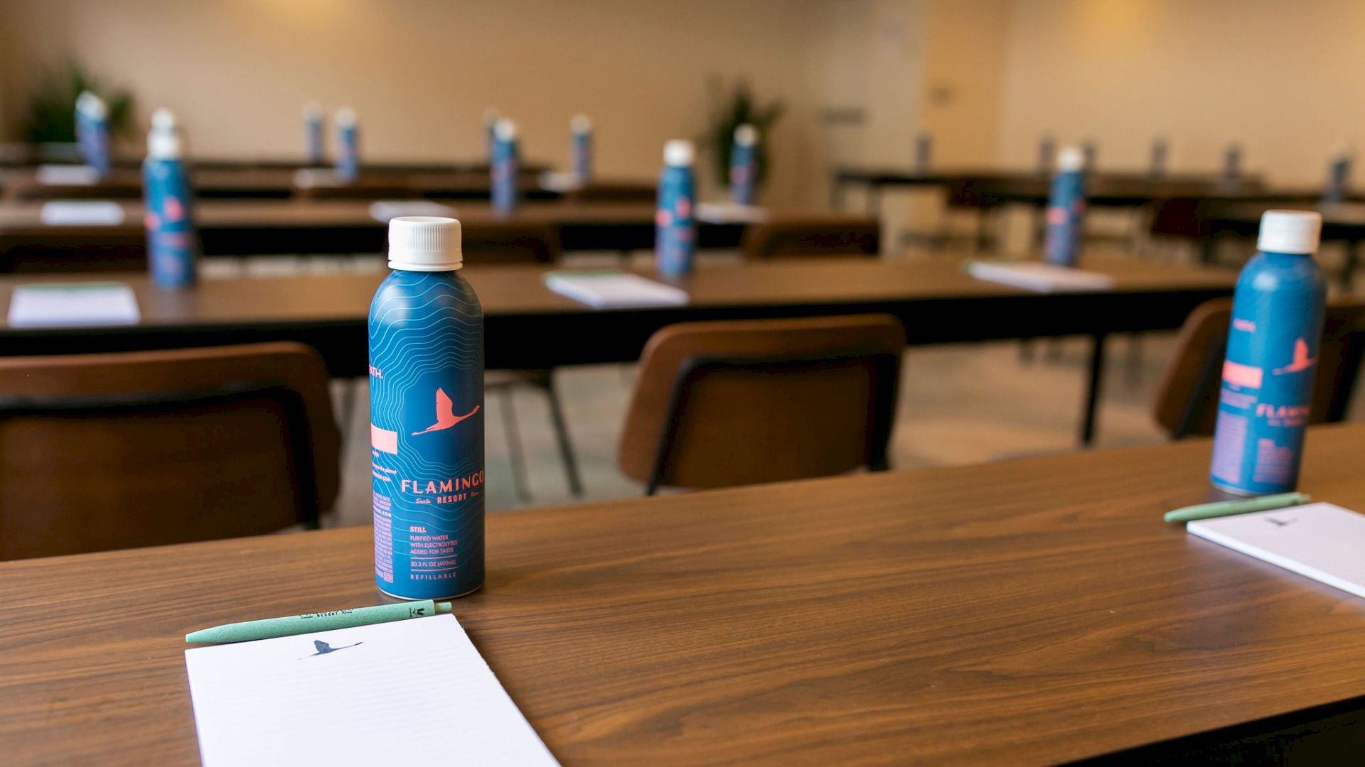 A conference room setup with tables and chairs featuring bottled water and notepads at each seat, ready for attendees.