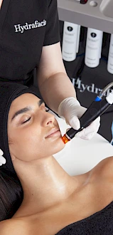 A person is receiving a HydraFacial treatment, with an aesthetician using a specialized device on their face.