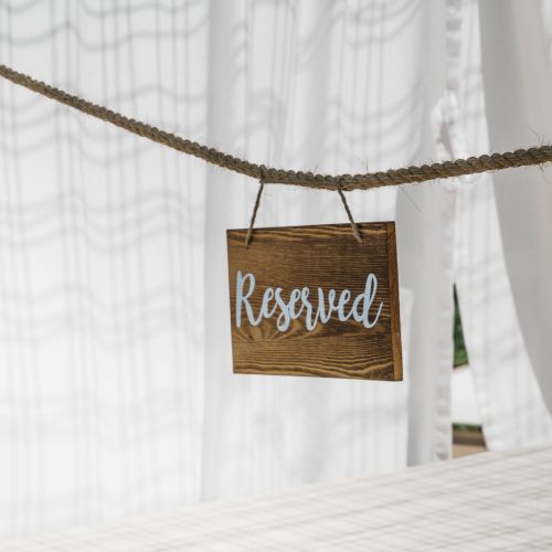 A wooden sign with the word "Reserved" hangs from a rope in front of a background of white curtains.