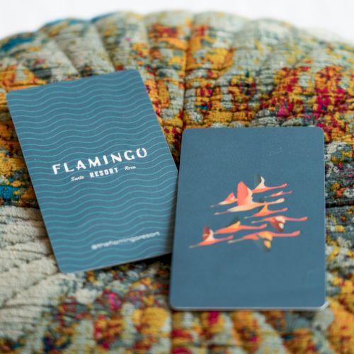 The image shows two cards placed on a textured surface. One card reads "Flamingo Resort" while the other features a design of flamingos.
