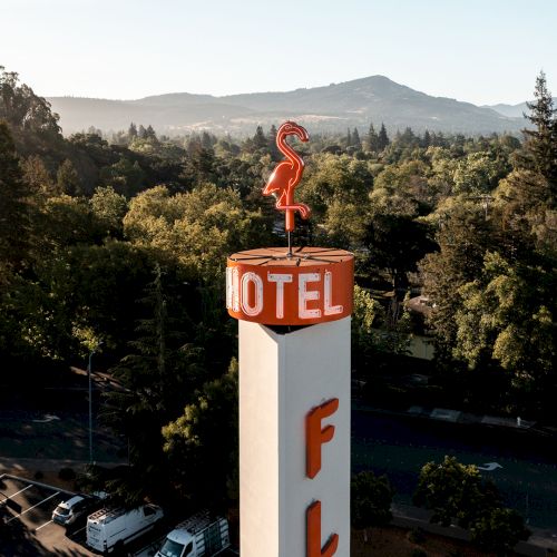 The image shows a cylindrical motel sign with a red flamingo on top and the word "MOTEL" written. The background has trees and a mountain.
