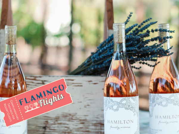 Three wine bottles labeled "HAMILTON" are displayed with a wooden box and flowers, featuring a "Flamingo Flights" tag beside them.