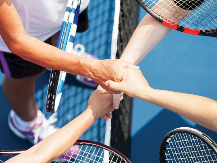 Tennis players shaking hands over the net, holding rackets, on a blue court.
