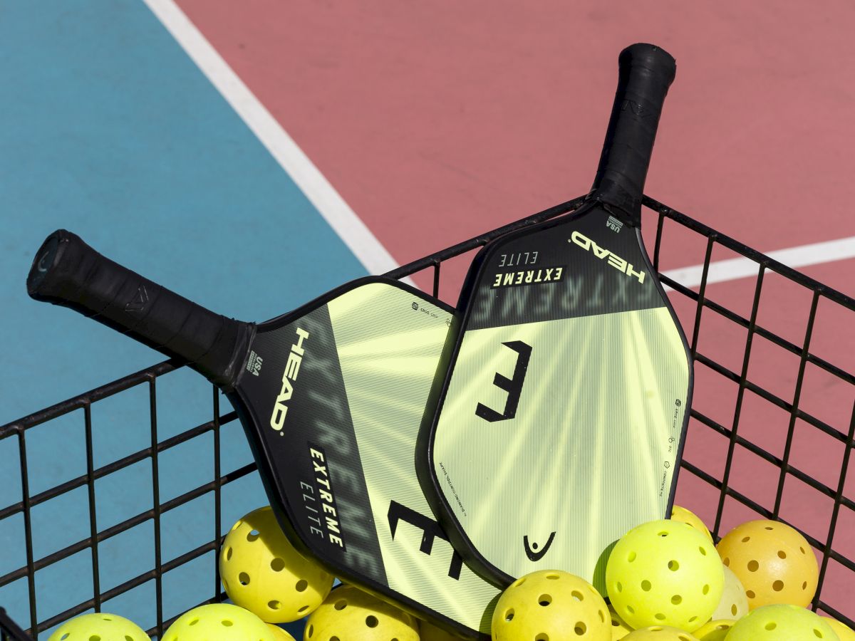 A tennis paddle resting on a basket of yellow tennis balls at a court, ready for practice.