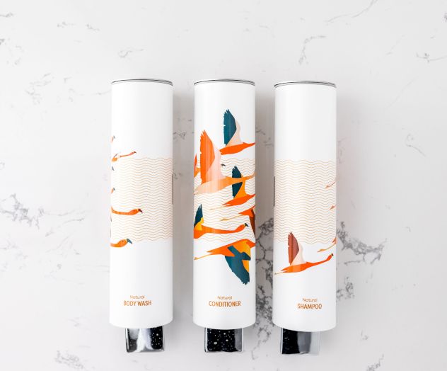 Three white cylindrical bottles with abstract orange and blue designs on a white marble surface.
