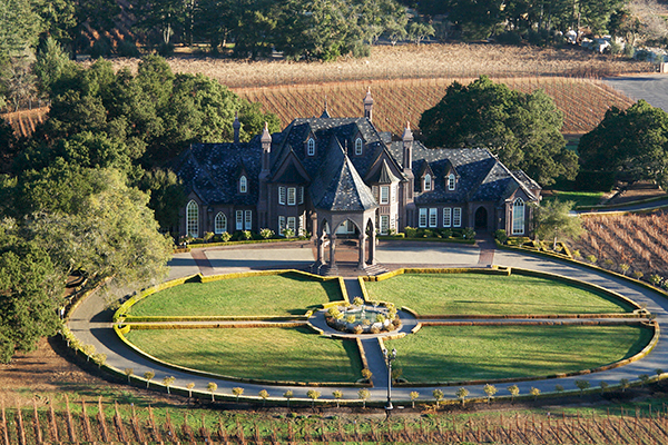 The image shows a large, castle-like mansion surrounded by vineyards, with a circular driveway and landscaped garden in front.