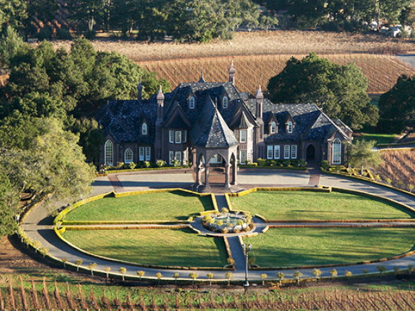 The image shows a large, castle-like mansion surrounded by vineyards, with a circular driveway and landscaped garden in front.