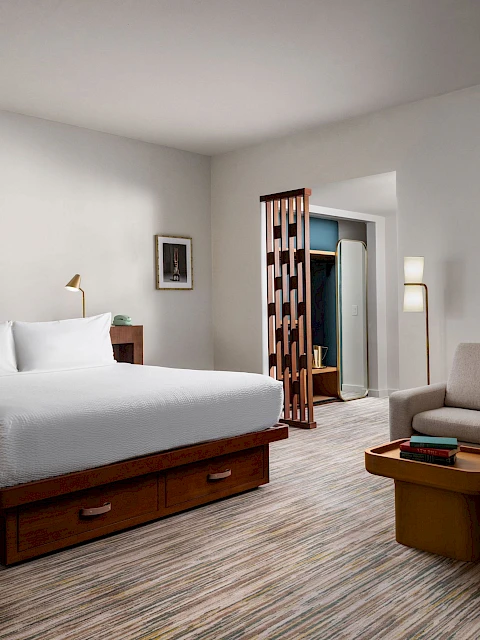 A modern hotel room with a bed, seating area, and decor on the walls, featuring neutral tones and contemporary furnishings.