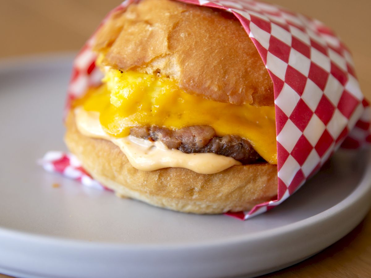 A cheese-and-egg breakfast sandwich with a sausage filling in a red-and-white wrapper.