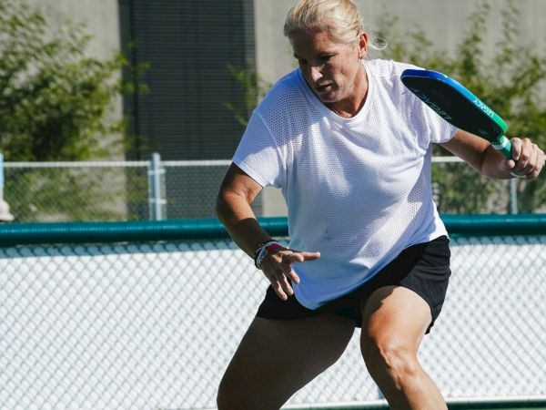 An older man in a white tee and black shorts plays tennis on a blue court, ready to swing with a paddle, focused and athletic.