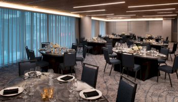 A banquet hall with round tables set for an event, featuring elegant place settings, black napkins, and floral centerpieces, under modern lighting.