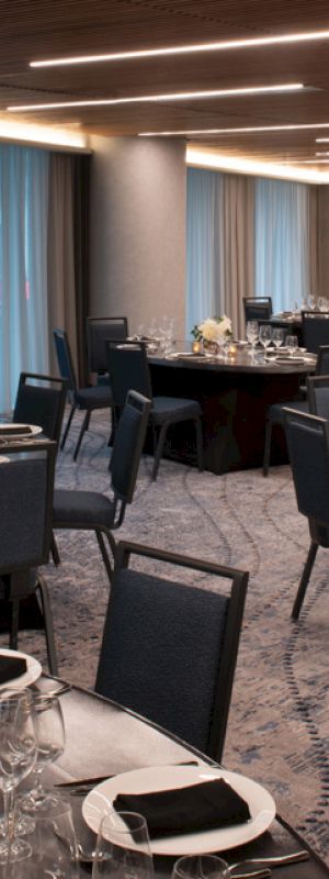 The image shows an elegant conference room with round tables set for a formal event, adorned with tableware and floral centerpieces.