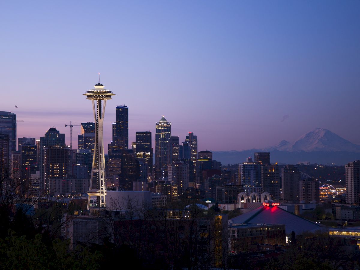 The image features the Seattle skyline at dusk, including the Space Needle and Mount Rainier in the distance, against a clear evening sky.