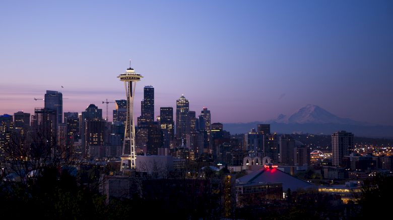 The image features the Seattle skyline at dusk, including the Space Needle and Mount Rainier in the distance, against a clear evening sky.