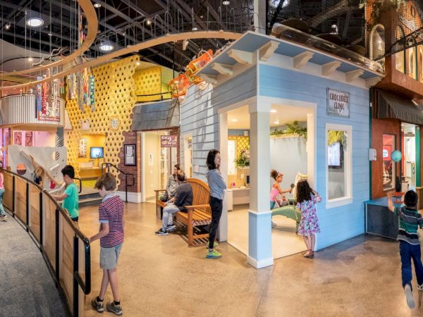 An indoor children&rsquo;s playground with kids playing near colorful tunnels, slides, and themed exhibits in a bright interactive space.